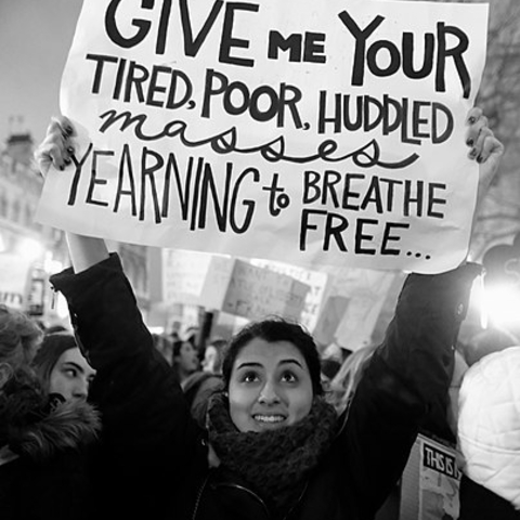 A protestor in London holds a sign with an excerpt from the poem 'The New Colossus.'